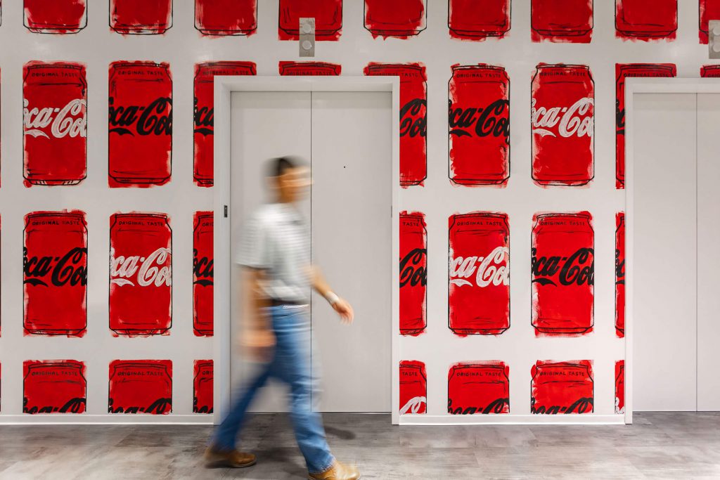 A wall covered with artistic paintings of Coca Cola cans